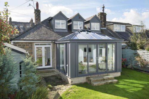 Anthracite grey orangery with a glazed lantern roof and solid base on a stone home