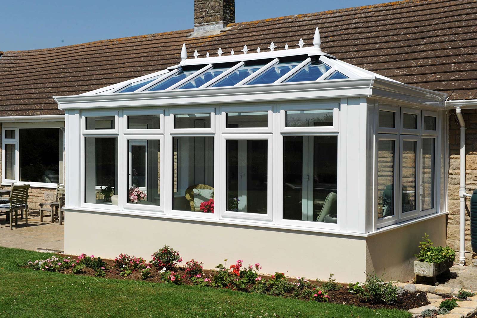 White orangery with a glazed lantern roof and rendered base overlooking a garden